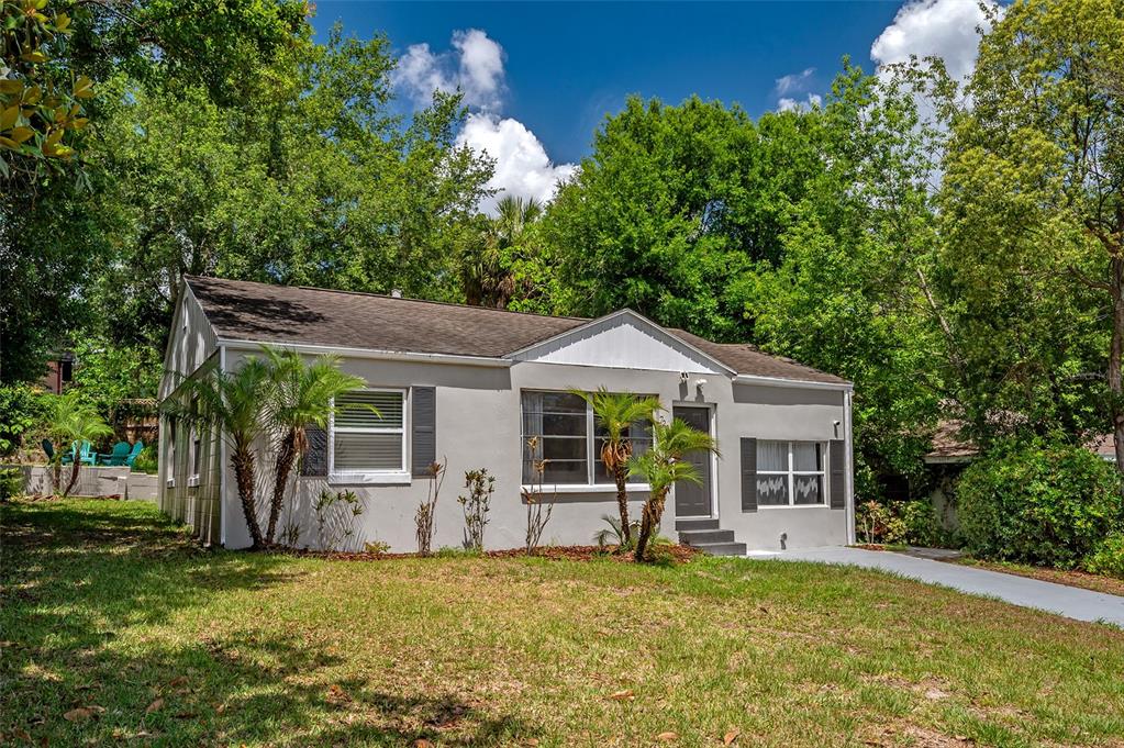 A single-story gray house with a gabled roof sits on a grassy lot with trees — 7204 N 15TH STREET, TAMPA, FL