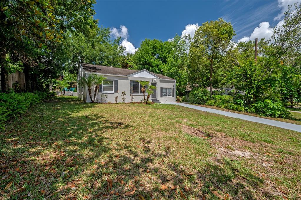 A single-story house with a light-colored exterior sits on a grassy lot with trees — 7204 N 15TH STREET, TAMPA, FL
