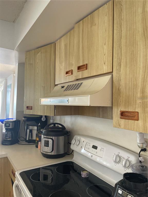 A kitchen features wood-grain cabinets, a white range hood, and a black electric stovetop — 5279 ISLA KEY BLVD UNIT 217, ST PETERSBURG, FL