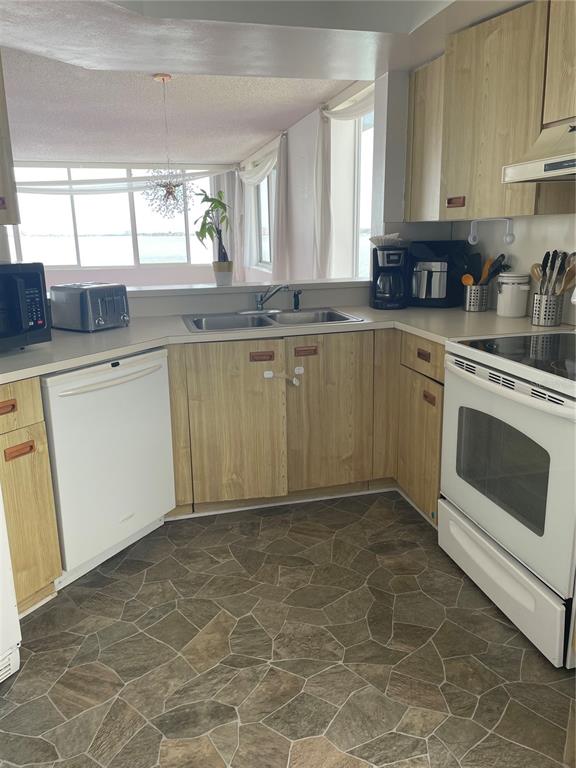 A kitchen features light wood cabinets, white appliances, and stone-patterned flooring overlooking a water view — 5279 ISLA KEY BLVD UNIT 217, ST PETERSBURG, FL