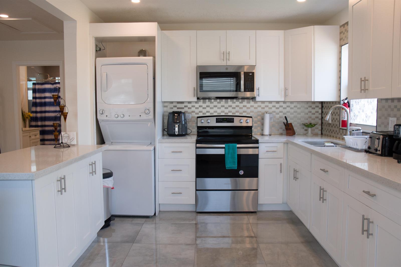 A kitchen featuring white cabinets, stainless steel appliances, a stacked washer-dryer unit, and tile flooring — 158 E 23rd Street, West Palm Beach FL 33404, WEST PALM BEACH, FL