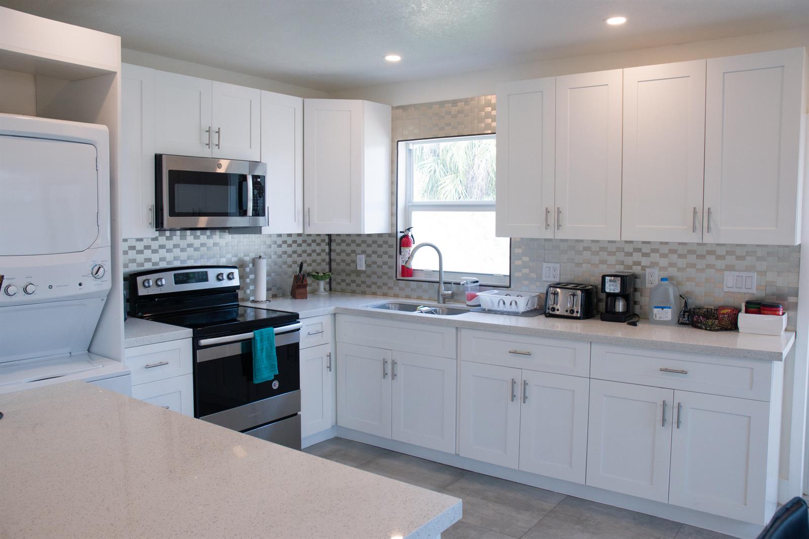 A kitchen with white cabinets, stainless steel appliances, a tiled backsplash, and quartz countertops — 158 E 23rd Street, West Palm Beach FL 33404, WEST PALM BEACH, FL
