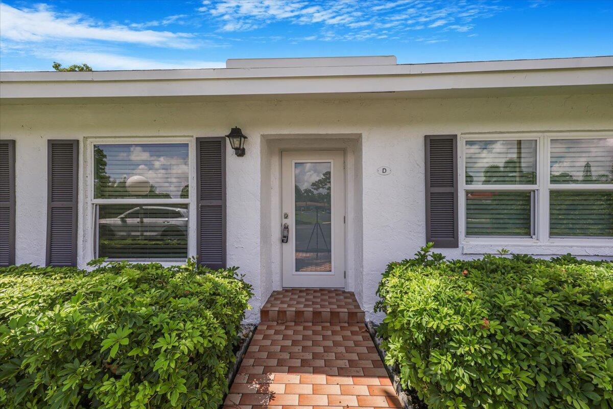 A white exterior wall features a front door labeled D, brick walkway, and green bushes — 5178 Privet Place # D, Delray Beach FL 33484, DELRAY BEACH, FL