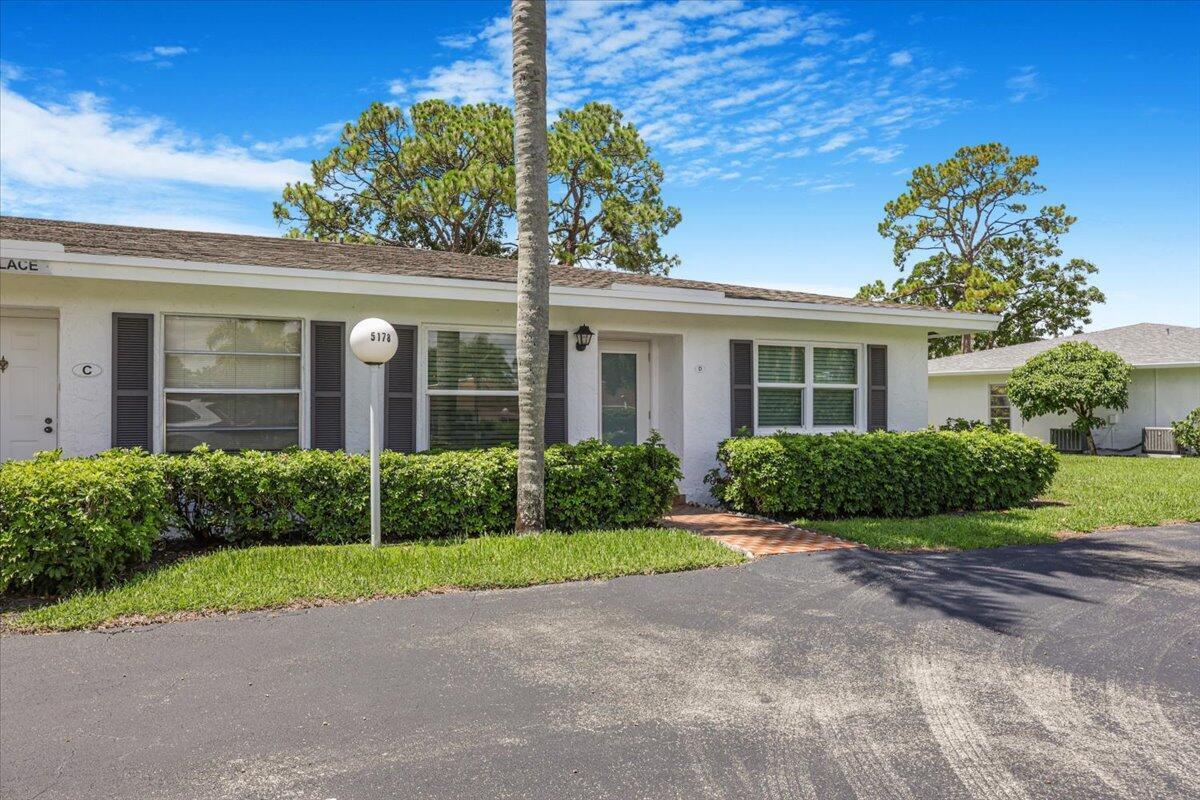 A single-story white stucco building features dark shutters, a front walkway, and manicured landscaping — 5178 Privet Place # D, Delray Beach FL 33484, DELRAY BEACH, FL
