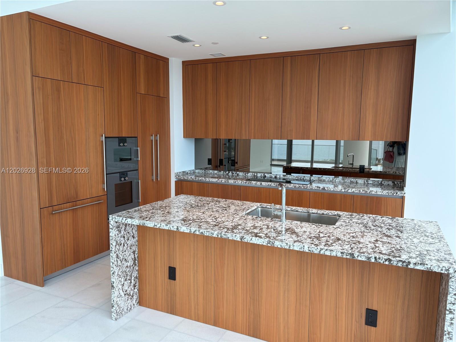 A modern kitchen features wood cabinetry, granite countertops, and a waterfall island with a sink — 175 SE 25 Road # 901, Miami FL 33129, MIAMI, FL