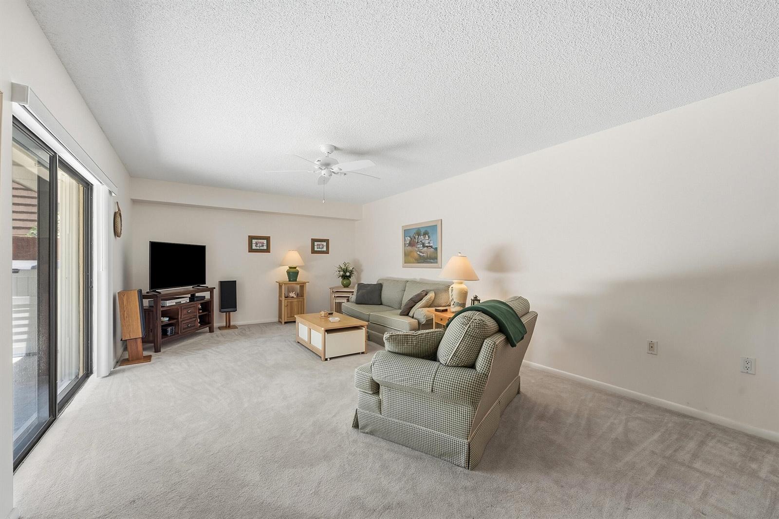 A living room features beige carpet, a ceiling fan, a sofa, an armchair, and a television — 2716 27th Court, Jupiter FL 33477, JUPITER, FL