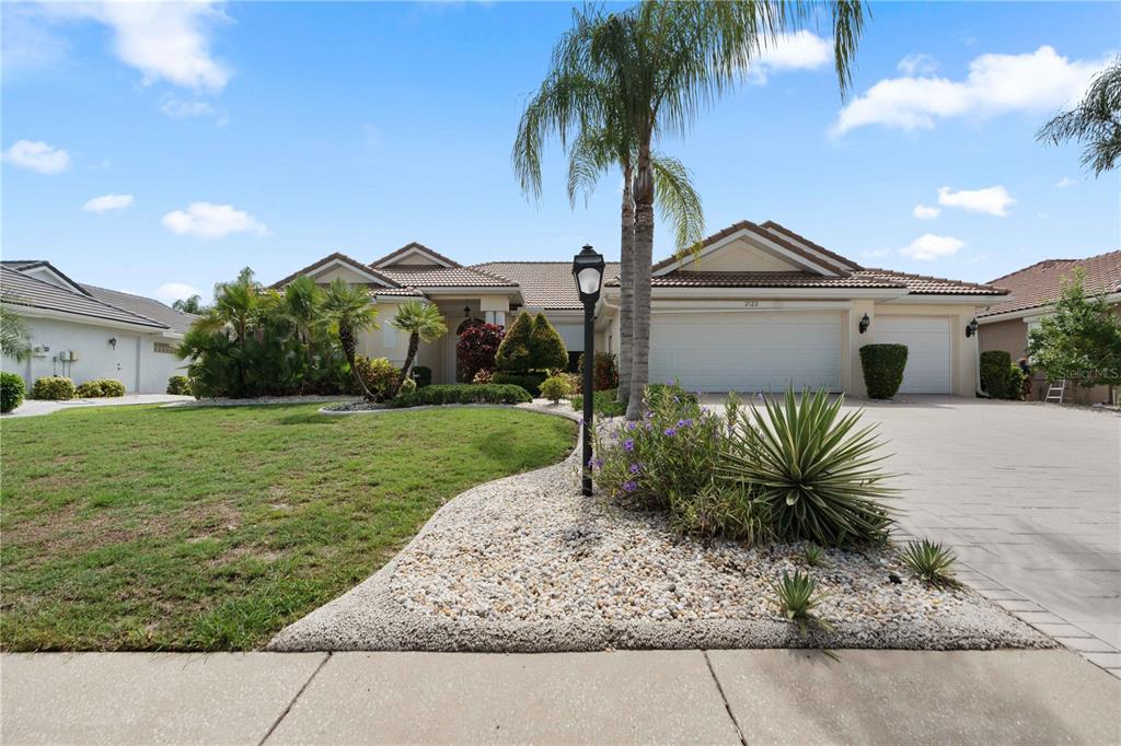 A single-story house with a tiled roof, a three-car garage, and a landscaped front yard — 2122 PLATINUM DRIVE, SUN CITY CENTER, FL