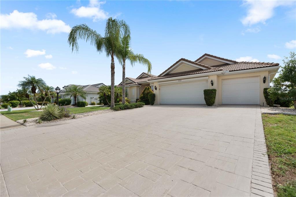A beige house with a three-car garage and a paved driveway under a blue sky — 2122 PLATINUM DRIVE, SUN CITY CENTER, FL