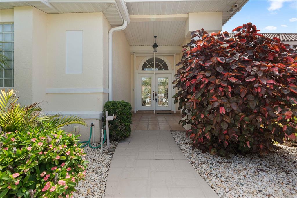 A paved walkway leads to the double front doors of a house with landscaping — 2122 PLATINUM DRIVE, SUN CITY CENTER, FL