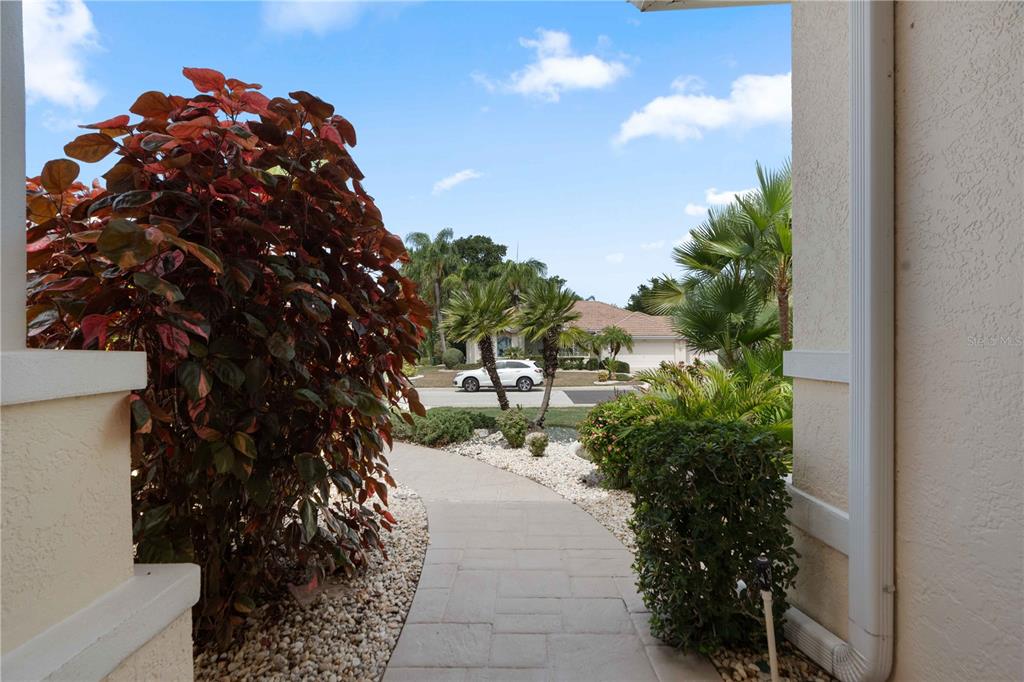 A paved walkway leads from a covered entryway toward a street with palm trees — 2122 PLATINUM DRIVE, SUN CITY CENTER, FL