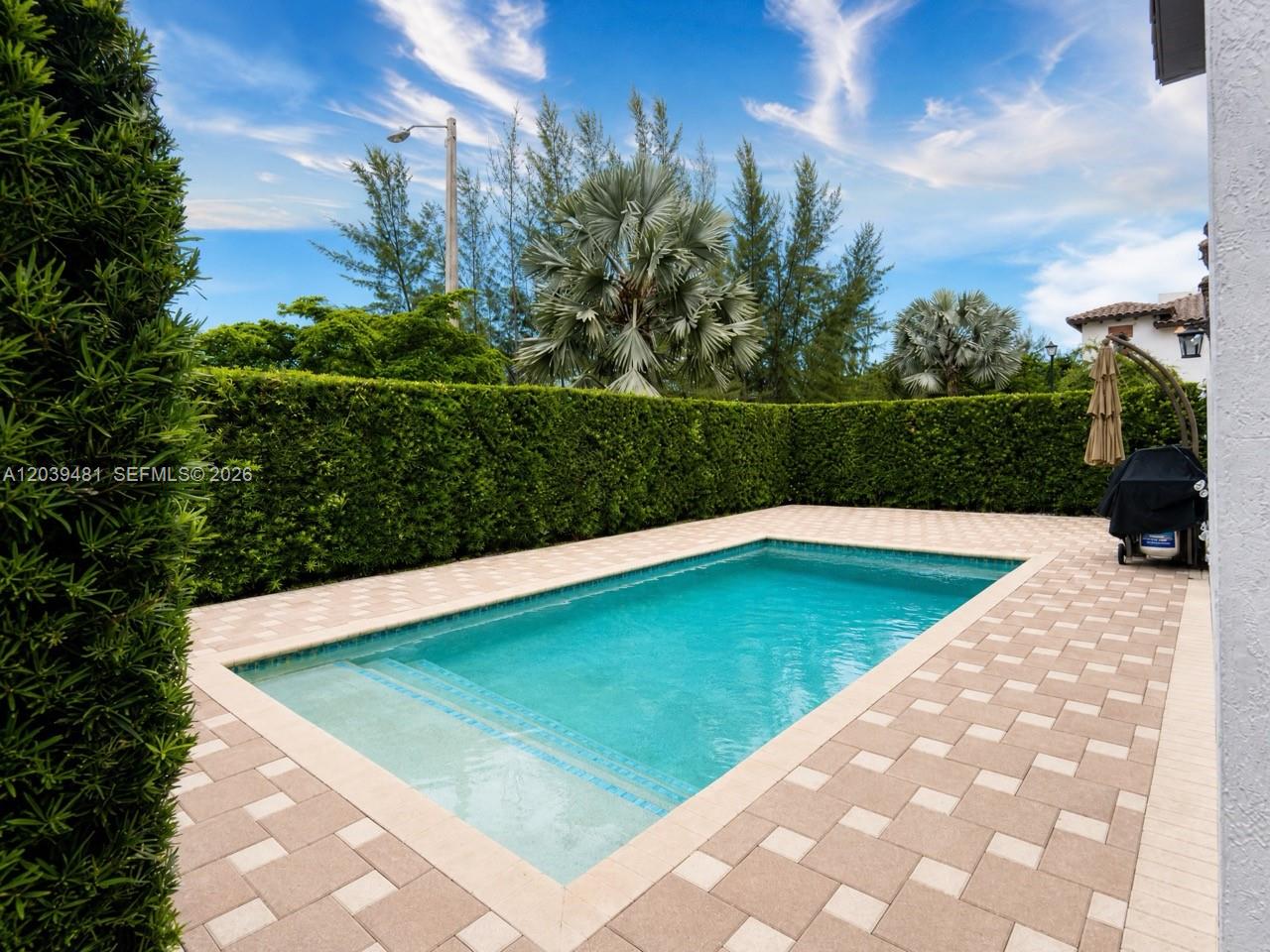 A rectangular swimming pool is surrounded by a paved patio and a tall green hedge — 8605 NW 102nd Ct, Doral FL 33178, DORAL, FL