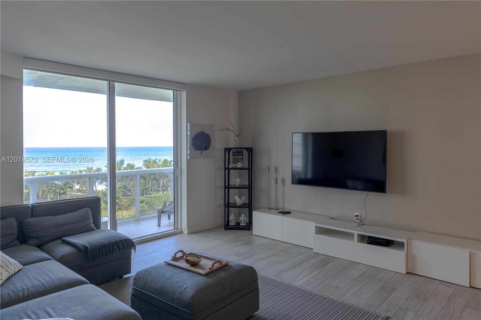 A living room features a gray sectional, a wall-mounted television, and a balcony overlooking ocean — 10275 Collins Ave # 634, Bal Harbour FL 33154, BAL HARBOUR, FL