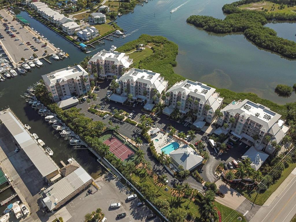 An aerial view shows a waterfront condominium complex with a pool, tennis court, and boat slips — 13113 GASPARILLA ROAD UNIT 405, PLACIDA, FL
