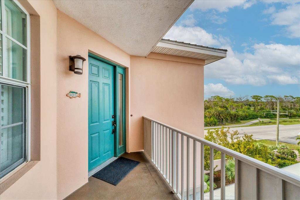 An exterior view of a balcony featuring a teal front door and white metal railing — 13113 GASPARILLA ROAD UNIT 405, PLACIDA, FL