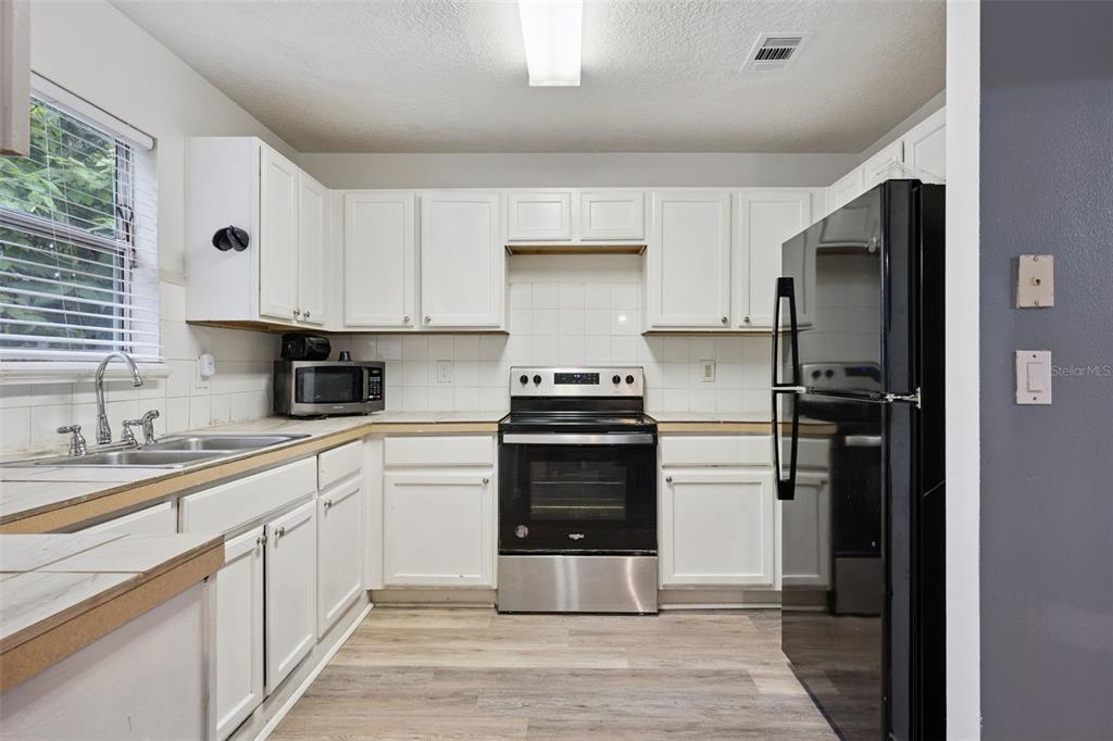 A kitchen features white cabinets, a black refrigerator, a stainless steel stove, and tiled countertops — 4532 HUPPEL AVENUE, ORLANDO, FL