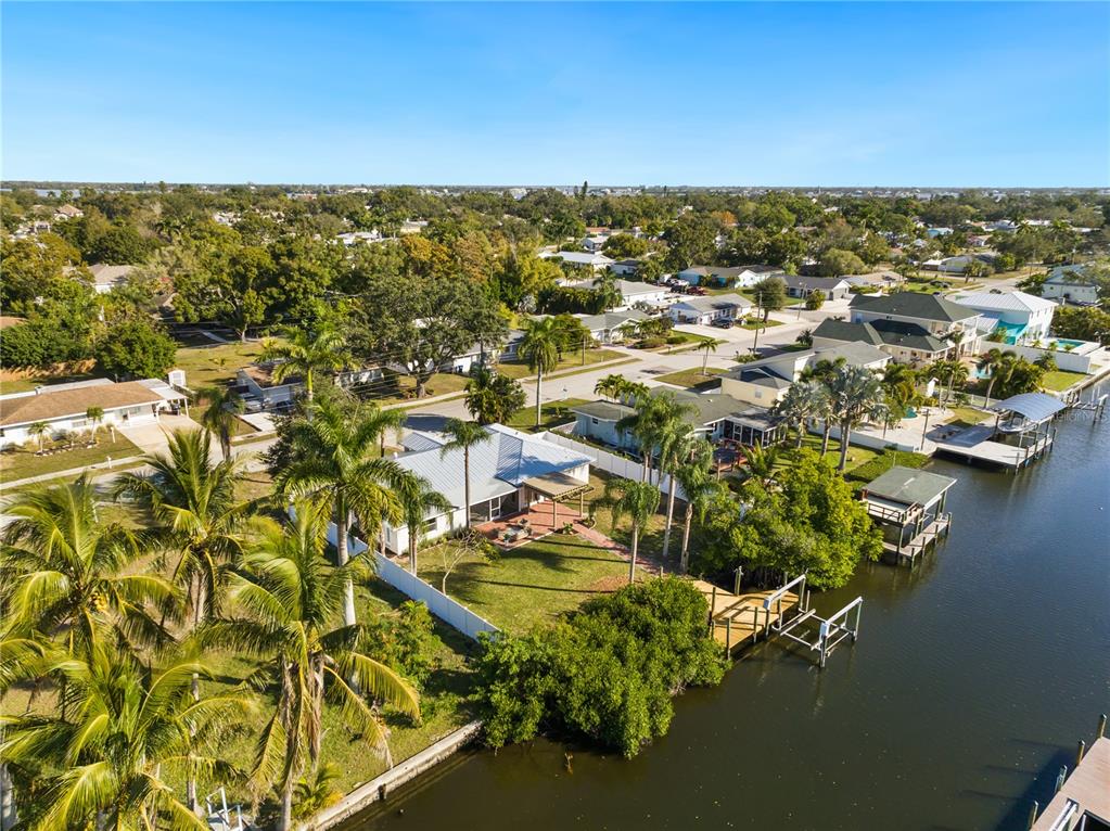 An aerial view shows a waterfront house with a backyard, palm trees, and a dock — 6911 9TH AVENUE NW, BRADENTON, FL