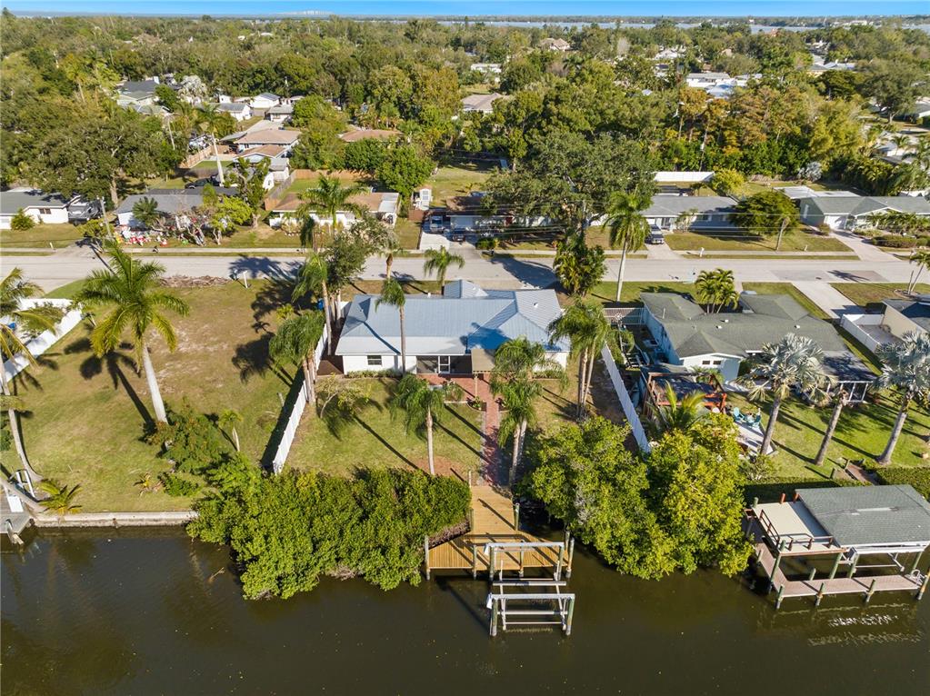 An aerial view shows a waterfront house with a metal roof, dock, and palm trees — 6911 9TH AVENUE NW, BRADENTON, FL