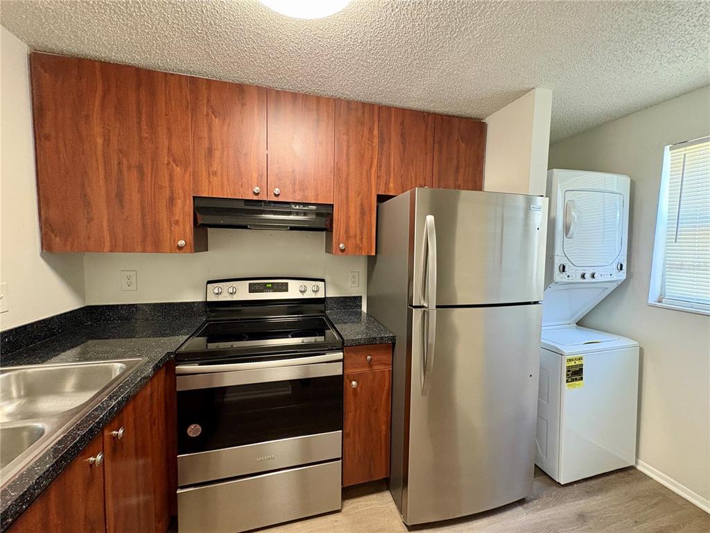 A kitchen features wood cabinets, stainless steel appliances, dark countertops, and a stacked laundry unit — 409 57TH AVENUE DRIVE E UNIT A, BRADENTON, FL