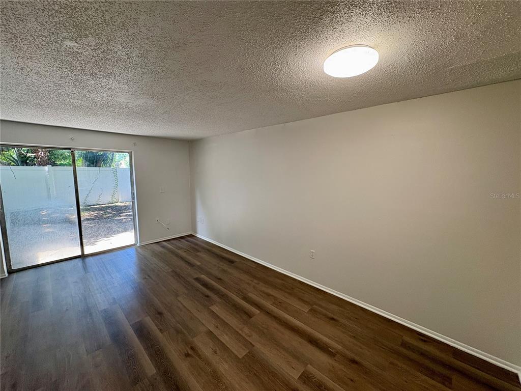 An empty room features wood-look flooring, a textured ceiling, a light fixture, and sliding glass doors — 409 57TH AVENUE DRIVE E UNIT A, BRADENTON, FL