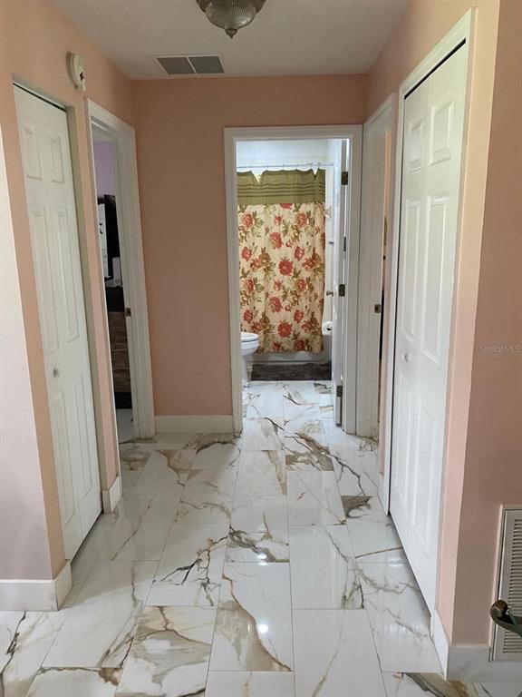 A hallway with white marble-look tile flooring leads to a bathroom with a floral shower curtain — 785 NW 67TH STREET, OCALA, FL