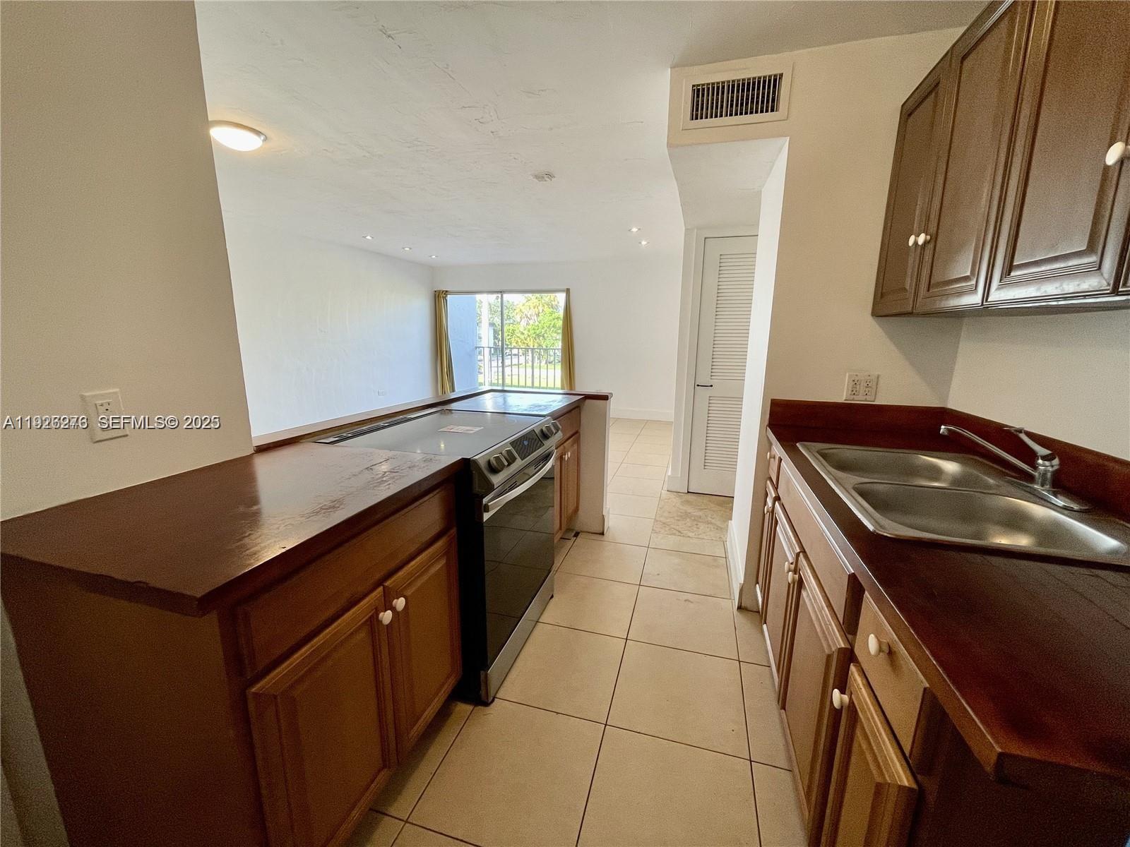 A kitchen with dark wood cabinets, laminate countertops, and tile flooring overlooks a living area — 7250 SW 94th Pl # B6, Miami FL 33173, MIAMI, FL