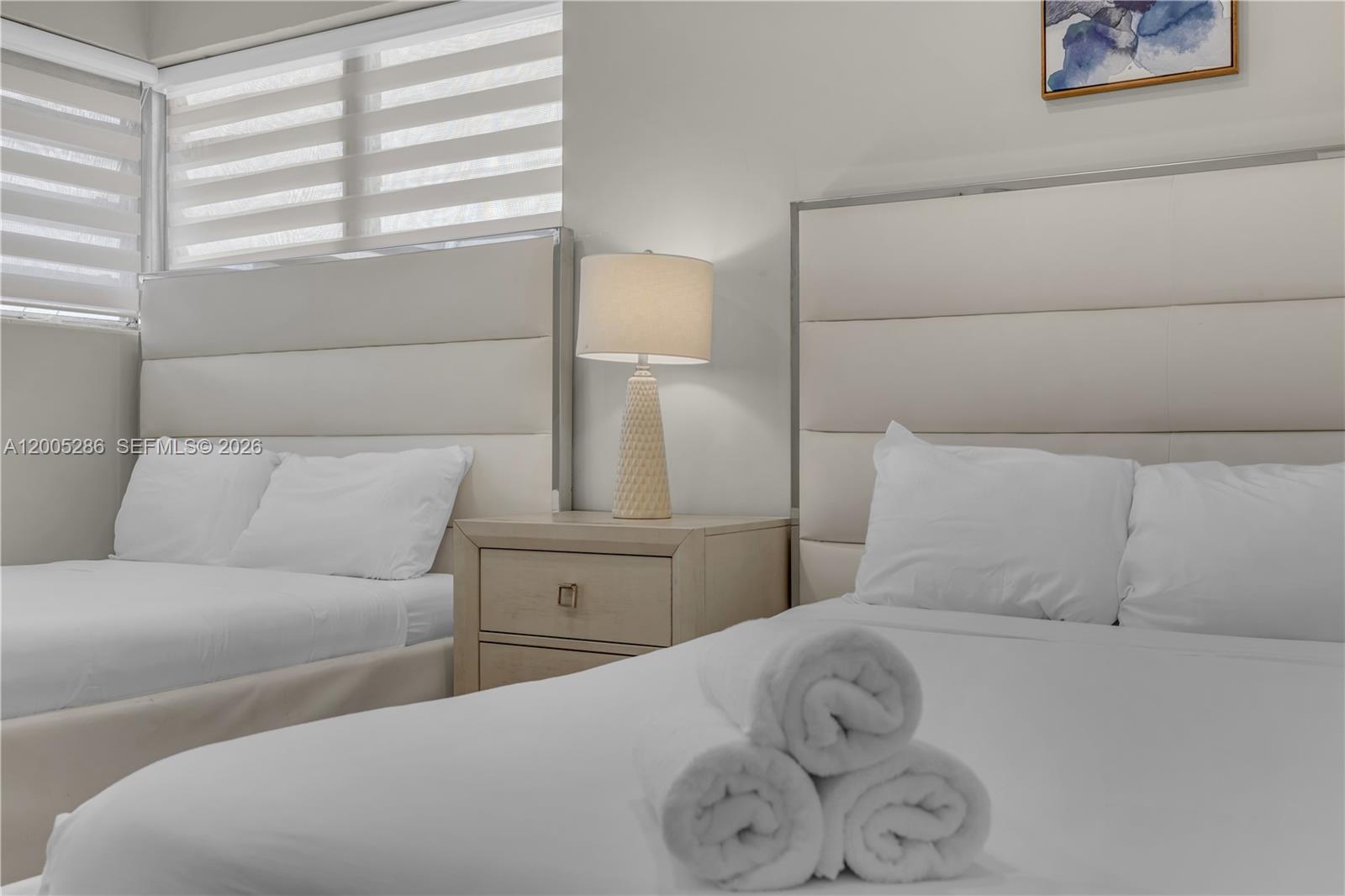 A bedroom features two beds with white headboards separated by a central nightstand and lamp — 10006 E Bay Harbor Dr # 15, Bay Harbor Islands FL 33154, BAY HARBOR ISLANDS, FL