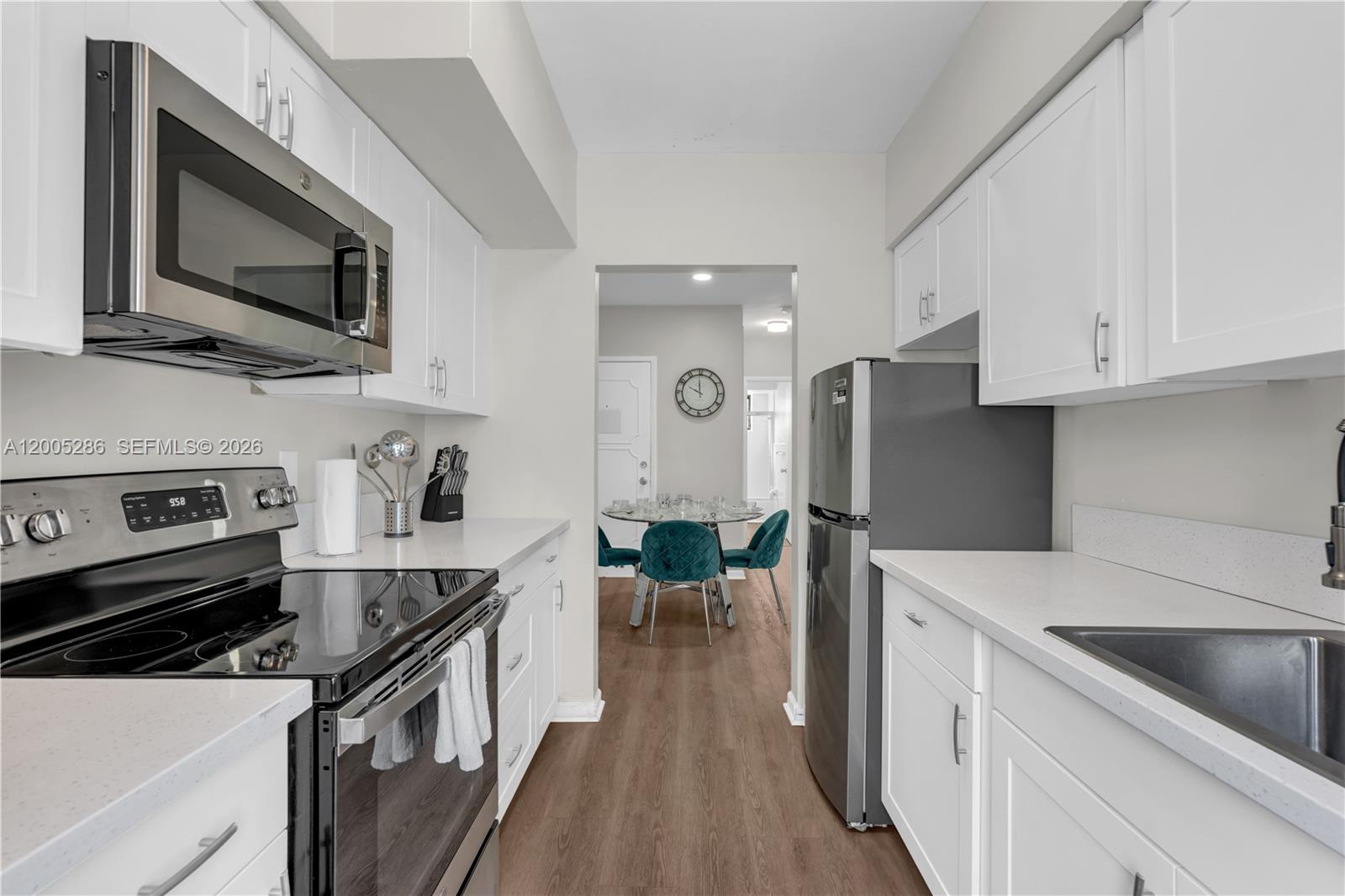 A galley kitchen features white cabinets, stainless steel appliances, and wood-look flooring — 10006 E Bay Harbor Dr # 15, Bay Harbor Islands FL 33154, BAY HARBOR ISLANDS, FL