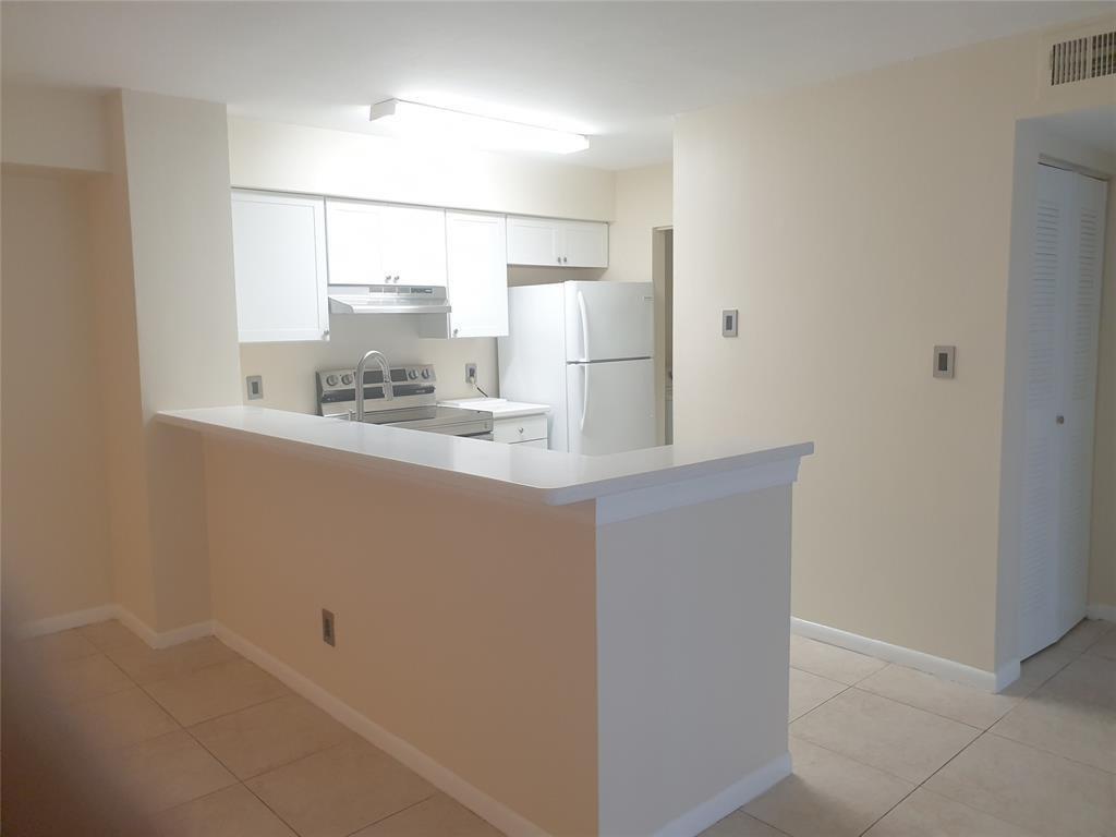 A kitchen features white cabinets, a white refrigerator, and a breakfast bar with tile flooring — 520 S Park Road # 12, Hollywood FL 33021, HOLLYWOOD, FL