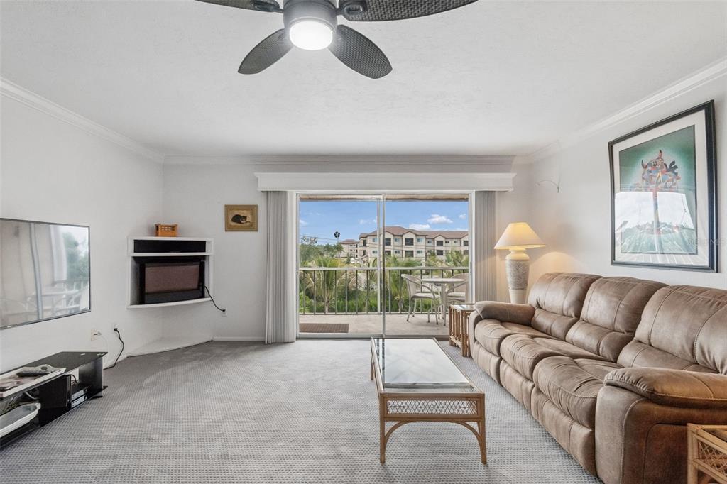 A living room with gray carpet, a brown sofa, a corner fireplace, and a balcony view — 1714 69TH AVENUE W UNIT C401, BRADENTON, FL