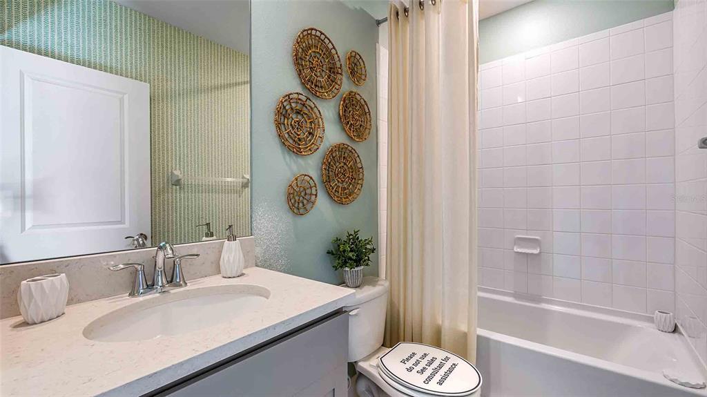 A bathroom features a vanity with a stone countertop, a tiled tub-shower, and wall decor — 18211 THISTLEBERRY PLACE, LAKEWOOD RANCH, FL