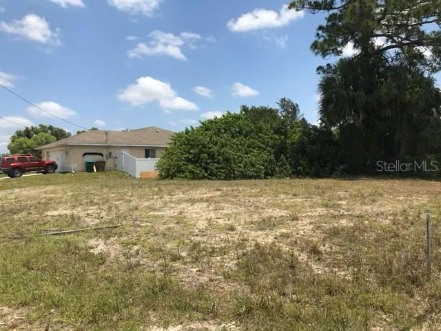 A vacant, grassy lot sits in front of a single-story house and large trees — 215 SW 9TH PLACE, CAPE CORAL, FL