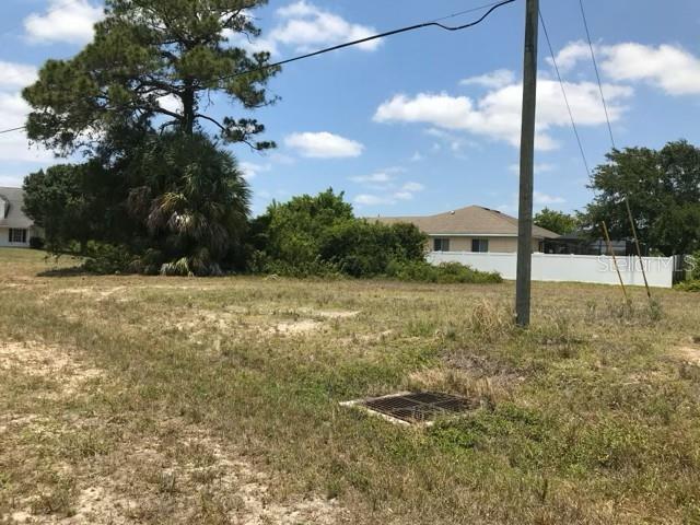 A vacant, grassy lot features a utility pole, a storm drain, and surrounding trees and houses — 215 SW 9TH PLACE, CAPE CORAL, FL