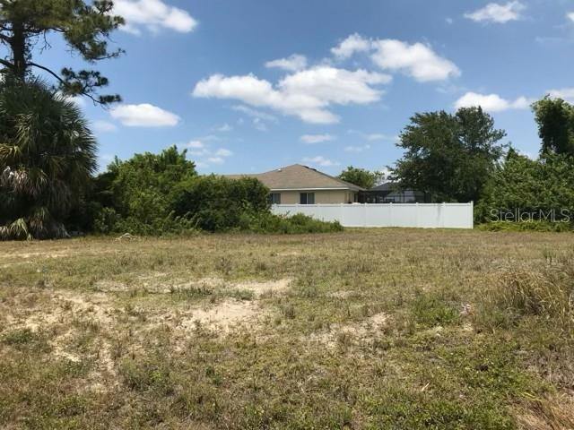 A vacant, grassy lot sits in front of a house with a white vinyl fence — 215 SW 9TH PLACE, CAPE CORAL, FL