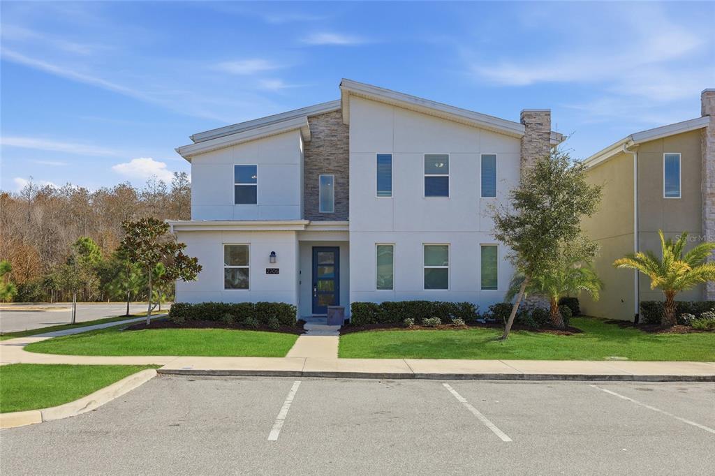 A two-story modern townhouse with white siding, stone accents, and a blue front door — 2706 OXYMORON WAY, KISSIMMEE, FL