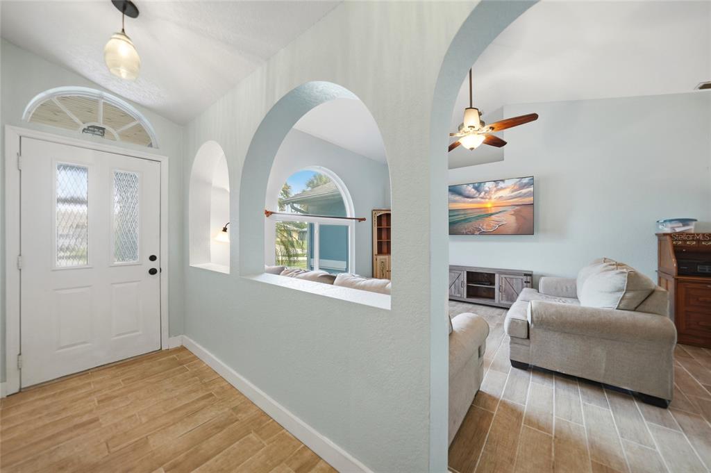 An entryway with arched cutouts leads into a living room featuring light tile flooring — 1632 AMSTEAD STREET, PORT CHARLOTTE, FL