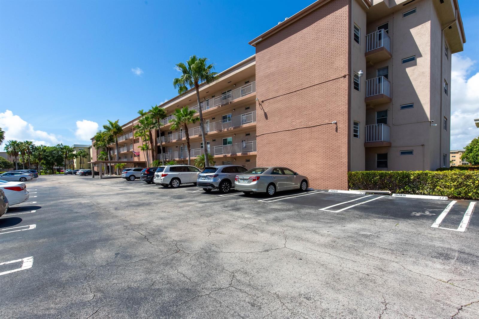 A multi-story brick apartment building features balconies and a parking lot with several cars — 2615 NE 1st Court # 411, Boynton Beach FL 33435, BOYNTON BEACH, FL