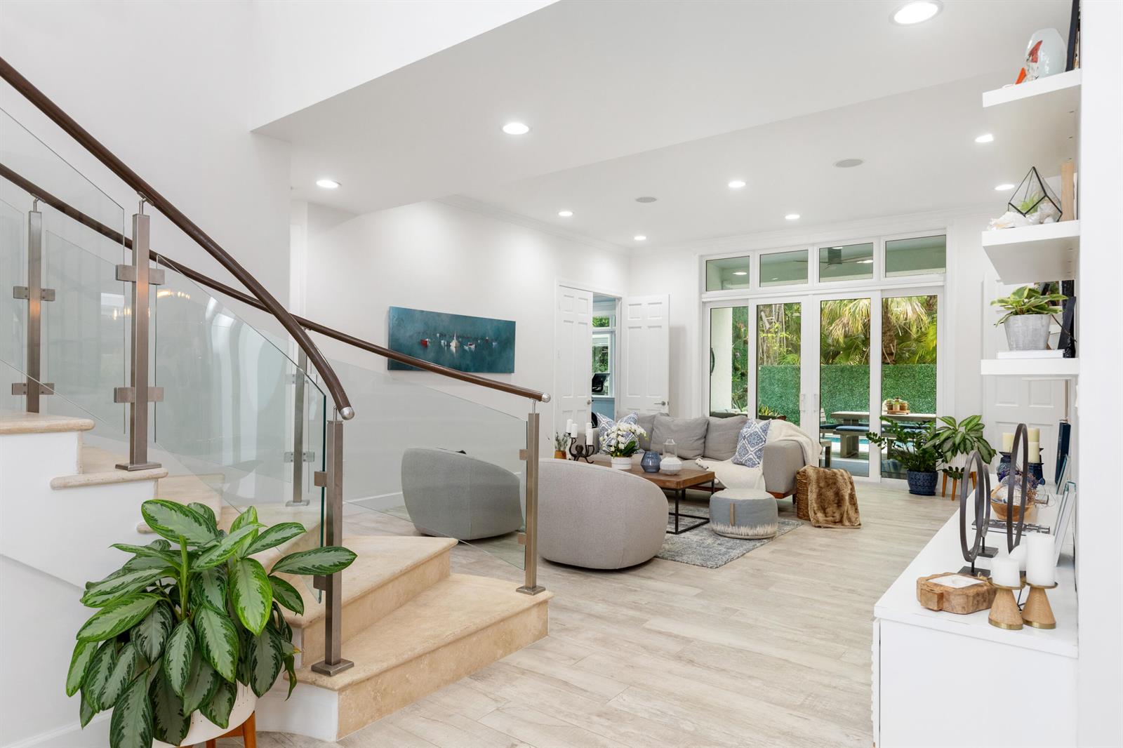 A modern living room features a curved glass staircase, light wood flooring, and patio doors — 24 Grand Bay Estates Circle, Key Biscayne FL 33149, KEY BISCAYNE, FL