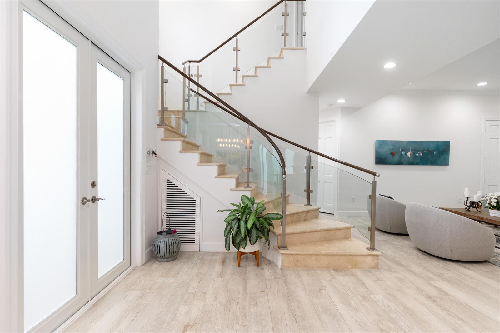 A bright entryway features a curved staircase with glass railings and light-colored wood flooring — 24 Grand Bay Estates Circle, Key Biscayne FL 33149, KEY BISCAYNE, FL