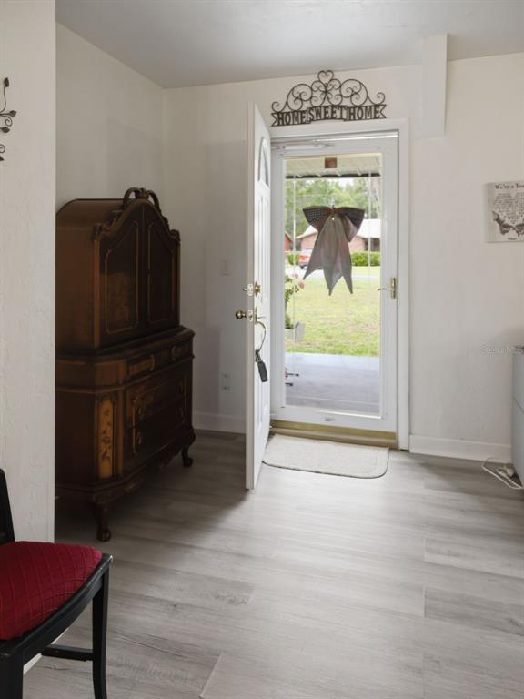 An entryway features light wood-look flooring, a dark wooden cabinet, and an open front door — 334 7TH WAY, INTERLACHEN, FL