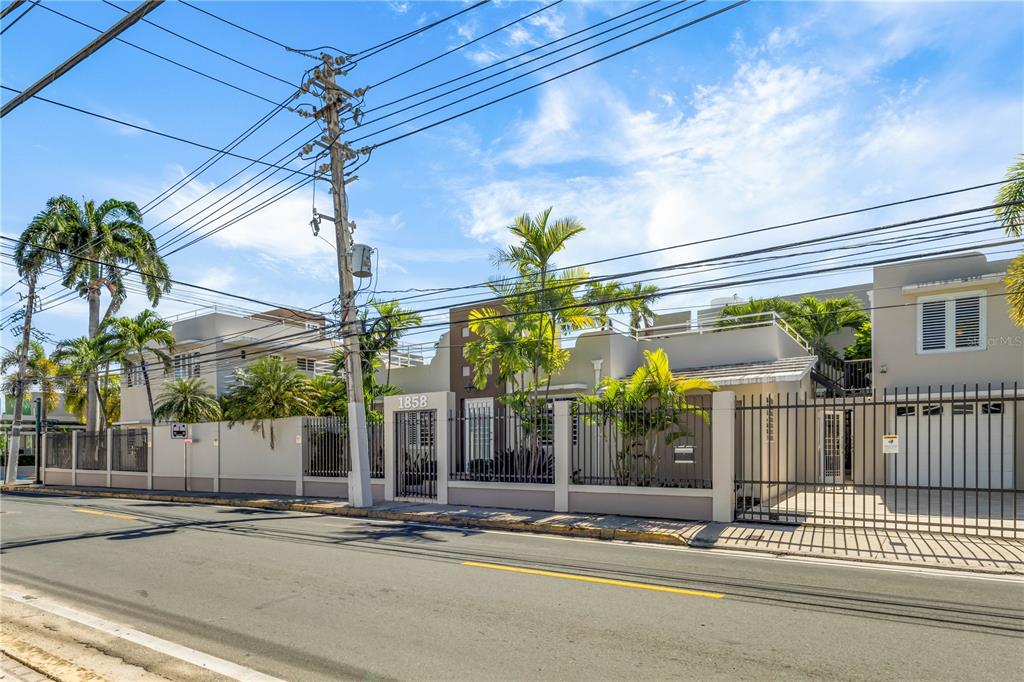 A tan, multi-level building with a gated courtyard and palm trees sits along a street — 1858 MCLEARY, SAN JUAN, PR
