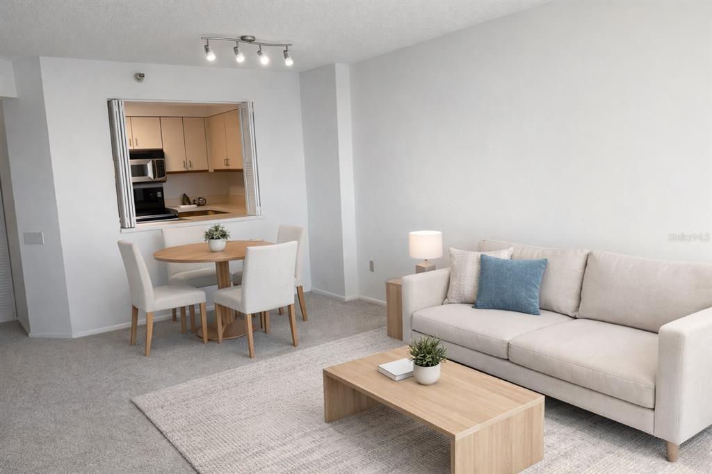 A living room and dining area with neutral furniture, carpeted floors, and a kitchen pass-through window — 2333 FEATHER SOUND DRIVE UNIT B304, CLEARWATER, FL