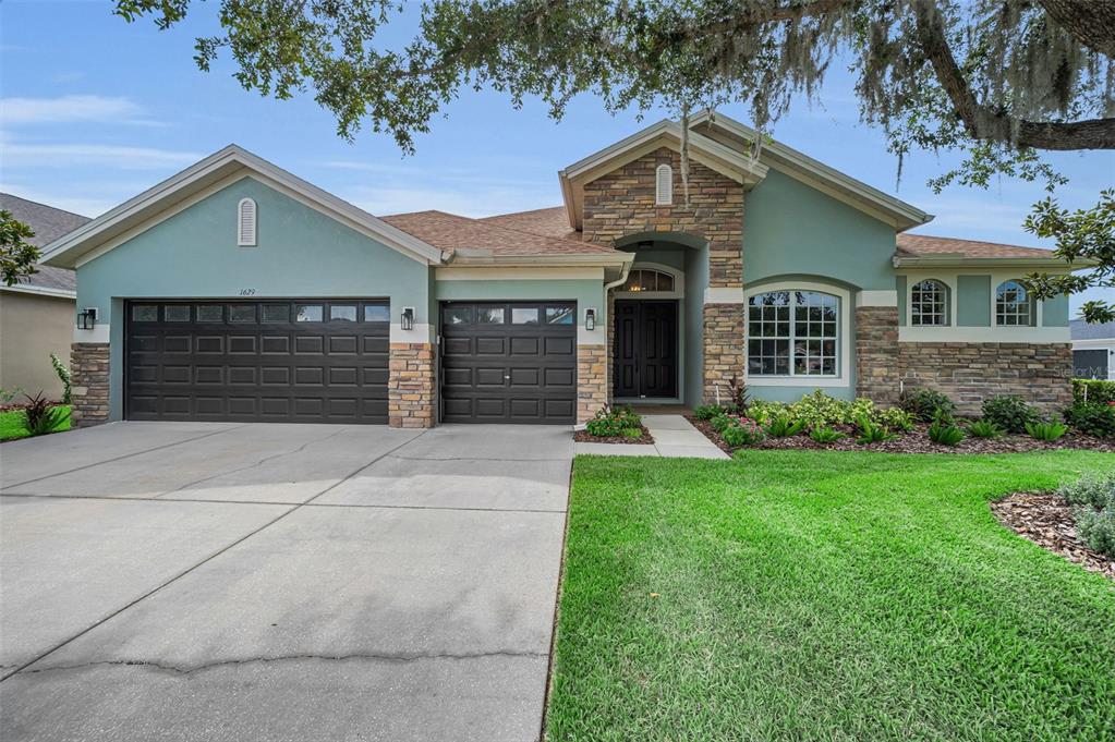 A single-story house with a teal stucco exterior, stone accents, and a three-car garage — 1629 SALMONBERRY STREET, WESLEY CHAPEL, FL