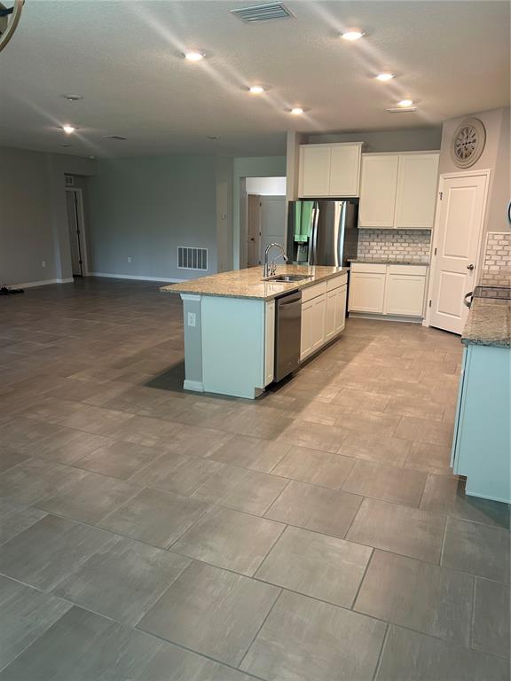 A kitchen with a granite-topped island and white cabinetry features gray tile flooring throughout — 7128 STEER BLADE DRIVE, ZEPHYRHILLS, FL
