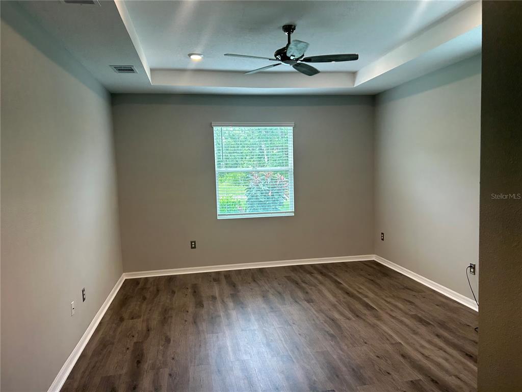 A bedroom with gray walls, wood-look flooring, a tray ceiling, and a ceiling fan — 7128 STEER BLADE DRIVE, ZEPHYRHILLS, FL