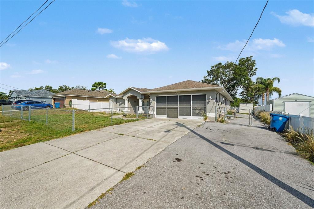 A single-story house with a screened garage and a concrete driveway under a blue sky — 4187 EVERETT AVENUE, SPRING HILL, FL