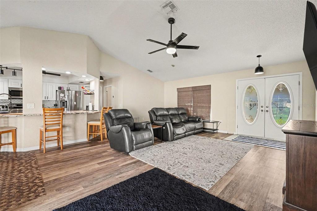 A living room with wood-look flooring, a ceiling fan, leather furniture, and an open kitchen — 4187 EVERETT AVENUE, SPRING HILL, FL