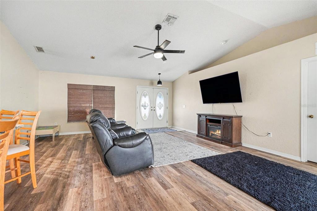 A living room features wood-look flooring, a vaulted ceiling, a ceiling fan, and a television — 4187 EVERETT AVENUE, SPRING HILL, FL