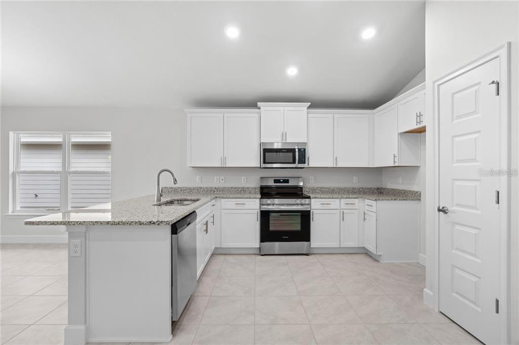 A kitchen features white cabinets, granite countertops, stainless steel appliances, and light tile flooring — 15 BIRCHWOOD DRIVE, PALM COAST, FL