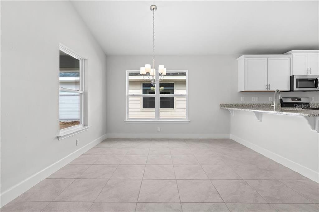 A dining area with light tile floors, a chandelier, and an adjacent kitchen breakfast bar — 15 BIRCHWOOD DRIVE, PALM COAST, FL