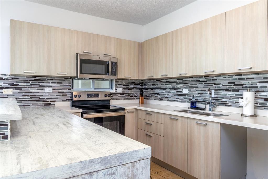 A kitchen features light wood cabinets, a textured countertop, and a multi-colored glass tile backsplash — PR-115 MAR AZUL CONDOMINIUM UNIT 2BN, AGUADA, PR